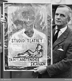 Das Bild zeigt eine Schwarz-Weiß-Fotografie von Øyvind Anker, der ein Plakat hält. Das Plakat zeigt eine Illustration: eine Person mit einem weißen Hemd, auf dem der Schriftzug „STUDIO TEATRET“ steht. Darunter ist eine weitere Figur gezeichnet – eine liegende Frau in einem Kleid. Der Text auf dem Plakat lautet: „STUDIO TEATRET“ „Jean-Paul Sartre“ „DEN ANSTENDIGE SKJØGEN“ „REGI AGNES MOWINCKEL“ Es handelt sich um eine Werbung für eine Theateraufführung des Studio Teatret, inszeniert von Agnes Mowinckel, basierend auf einem Werk von Jean-Paul Sartre.