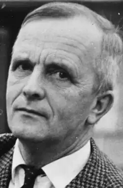 Das Bild zeigt ein Schwarz-Weiß-Foto von Øyvind Anker (2016). Er trägt eine karierte Jacke, ein weißes Hemd und eine dunkle Krawatte. Im Hintergrund ist eine Tafel zu sehen, was darauf hinweist, dass die Aufnahme möglicherweise in einem Klassenzimmer oder einem Büro gemacht wurde.