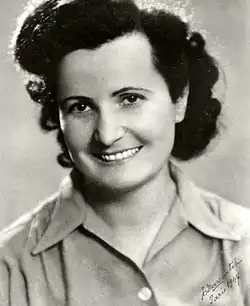 eine junge Frau mit dunklem, lockigem Haar und freundlichem, offenen Lächeln