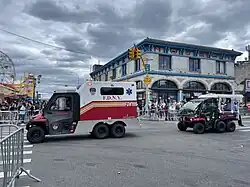 zwei dreiachsige Kleinfahrzeuge fahren hintereinander her, das vordere hat einen geschlossenen Kofferaufbau zum Personentransport, das hintere hat eine offene, aber überdachte Sitz- und Ladefläche.