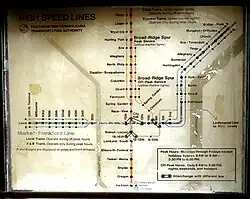 vergilbter Liniennetzplan zeigt kreuzförmiges U-Bahn-Netz. Grob horizontal eine blaue Linie mit einer vertikalen und dann diagonal nach rechts oben verlaufenden Fortsetzung. Vertikal eine orangefarbene Linie. Dazu dünne Hilfslinien. Stationen sind schematisch mit schwarzen Punkten markiert und serifenlos schwarz beschriftet. Schlecht erkennbare Überschrift "High Speed Line" links oben, Legende und Infobox rechts unten.