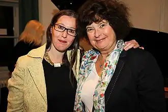 Das Billd ist im Querformat und zeigt zwei Frauen. Links steht Gabriele Proy die einen Arm um Carmen Ottner legt. Beide Frauen schauen lächelnd in die Kamera.