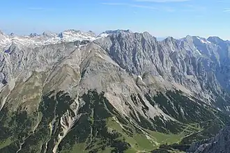 Gamskarspitze von der Speckkarspitze, der Gipfel ist etwas links von dem Gipfel der Grubenkarspitze dahinter (der etwas höhere Gipfel rechts ist die Brantlspitze). Der Anstieg verläuft von der Wiese in den Latschen in der linken unteren Bildecke Richtung Grat, dann rechts durch die seichte Mulde unterhalb des Grates Richtung Gipfel, zuletzt in Felsen am Grat