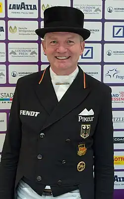 Das Foto zeigt das Gesicht des Dressurreiter Hubertus Schmidt. Er trägt einen schwarzen Zylinder und einen schwarzen Frack.