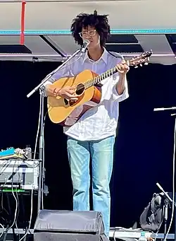 Foto eines Mannes, der mit Gitarre auf einer Bühne steht