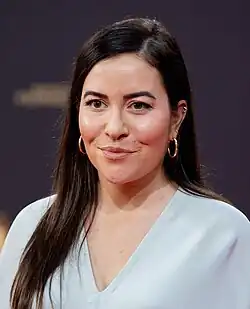 Aline Abboud beim Deutschen Fernsehpreis 2023. Sie trägt ein helles Oberteil und ein Paar Ohrringe sowie ihre langen, dunklen Haaren offen. Im dunkel gehaltenen Hintergrund ist verschwommen ein Schriftzug erahnbar.