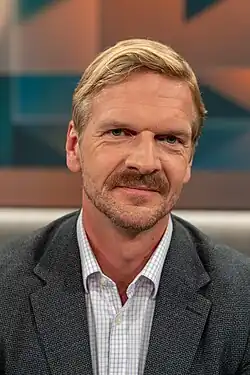 Porträt vor Fernsehkulisse "Hart aber fair"