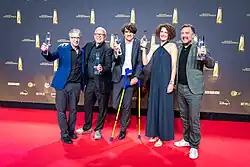Gruppenaufnahme mit Fernsehpreis-Trophäen auf einem roten Teppich vor einer Wand mit Senderlogos