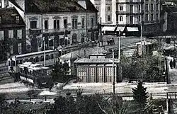Abfahrtsstelle der Vöslauer Linie am Josefsplatz, links ein aus Wien angekommener Zug der Badner Bahn, davor wartend ein grün-créme lackierter Wagen der Serie 92–99.