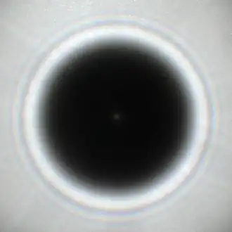 Fotografische Aufnahme des Beugungsmusters mit einem Poisson-Fleck in der Mitte im Schatten eines kreisförmigen Hindernisses mit 5,8 Millimeter Durchmesser in Licht einer ungefähr 0,5 Millimeter großen, ungefähr anderthalb Meter entfernten Lochblende mit Sonnenlicht aus ungefähr 1,8 Metern Entfernung.