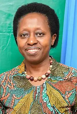 Lächelnde, mittelalte Frau mit kurzem Afrolook. Sie trägt bunte Kleidung mit Blättermuster und eine Halskette mit großen, verschiedenfarbigen Perlen.