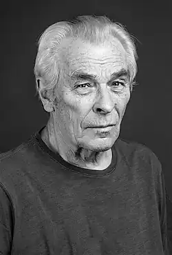 Alois Švehlík (2019) trägt weiße Haare und ein schlichtes, dunkel gefärbtes Hemd. Der Hintergrund des Bildes ist einfarbig dunkel, wodurch die Person des schwarz-weiß Fotos im Mittelpunkt steht.