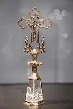 In einer Ausstellungsvitrine steht ein silber-goldenes Kruzifix mit einem sechseckigen Sockel aus Bergkristall. Rechts und links von dem eigentlichen Kreuz sind die trauernden Johannes und Maria angebracht.