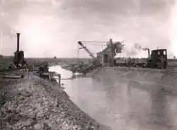 Schwarz-Weißbild eines Eimerbaggers der einen Fluss ausgräbt