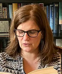 Die Autorin Bettina Hennig bei einer Lesung in Hamburg, sie trägt ein schwarz-graues Kleid, brünettes, schulterlanges Haar, Brille und schaut ins Buch und nicht in die Kamera