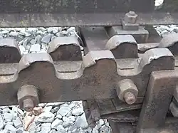 Ausschnitt von linkem Bild (vor zweiter Stangen-Lagerstelle): Zahnabnutzung durch die Bremszahnräder, die bei Einfahrt aufprallen, um auf Ein­fahrdrehzahl beschleunigt zu werden