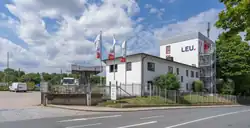 Das Foto zeigt die das Gebäude (rechts) mit Gelände, gesehen von der gegenüberliegenden Straßenseite