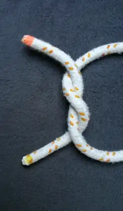 Das Bild 3 von oben um 90° im UZS gedreht. Ein „S“ geschlagener Halber Knoten (das Seil mit gelbem Ende zeigt den Buchstaben S).