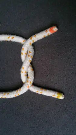 Das Bild 2 von oben um 90° im UZS gedreht. Ein „Z“ geschlagener Halber Knoten (Man betrachte die Stelle, an der ein Seil in der Mitte über das andere geht. Das Seil mit gelbem Ende zeigt den Buchstaben Z).