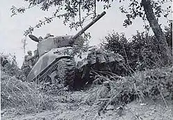 Ein Sherman-Panzer mit Culin Hedgerow Cutter an der Front durchquert eine Wallhecke