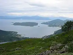 Foto von einer Anhöhe auf eine Bucht herunter, in der eine unbesiedelte Insel liegt. An der Küste entlang ist das Gebiet besiedelt.