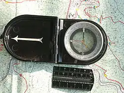 Kompass mit 400-Gon-Teilung und Umrechnungslineal (D&nbsp;= Degree&nbsp;= Grad, G&nbsp;= Gon, ″&nbsp;= Strich) mit Längenmaß in Millimeter