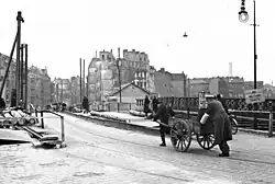 Ein Polizist hilft einem alten Mann, dessen schweren Wagen über eine Brücke zu schieben.