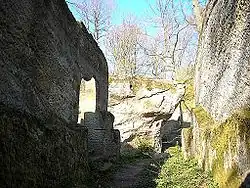 Gegenblick nach Nordosten mit dem Burgbrunnen unter dem Nordwestfelsen. In die Felswand sind Zulaufrinnen und Balkenlöcher der Brunnenstube eingearbeitet