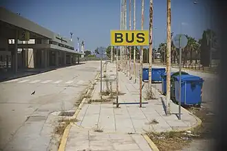 Busterminal mit dem im Hintergrund zu sehenden, unter Denkmalschutz stehenden Empfangsgebäude des ehem. internationalen Flughafens Ellinikon in Athen.
