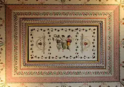 Farbige Deckenmalerei mit verschiedenen rechteckigen Rahmenmustern, in deren Mitte drei Frauen in antiken Kleidern tanzen. Beide äußeren Frauen greifen sich an den Händen und die mittlere Frau hält in ihren Händen zwei Kränze. Sie sind von zwei umrankten Stäben mit daran befestigten Stoffbögen und jeweils zwei zusammengebundenen Köpfen begrenzt. Die gesamte Szene wird von Lianen umschlossen.