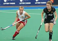 Chloe Rogers im weißen Trikot und mit rotem Rock sprintet gegen die deutsche Spielerin in schwarzer Spielkleidung.