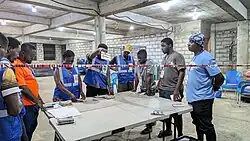 Ein Raum mit neun um einen Tisch mit Stimmzetteln versammelten Personen.