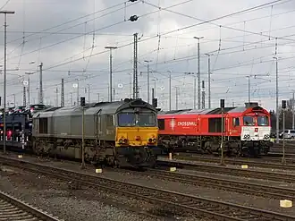 Zwei Crossrail-Diesellokomotiven in unterschiedlichen Farbvarianten. Vorn in silber-gelb eine Class 66, dahinter in roter Lackierung eine Class 77, die sich von der Class 66 durch die Klimageräte über den Führerständen gut unterscheiden lässt.