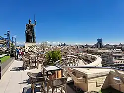 Auf der Terrasse sind Tische und Stühle, das Panorama der Stadt zeichnet sich ab.