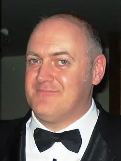 Das Foto zeigt Dara Ó Briain im Porträt während der BAFTA-Zeremonie 2011. Er ist in einem schwarzen Anzug mit Fliege gekleidet.