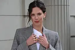 Delfina Chaves in einer Aufnahme von 2025 in grauem Blazer, die braunen Haare hochgesteckt und rechts mit einer Strähne, die herabgerutscht wirkt