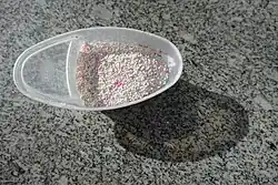 Weiße und rosane Kügelchen in einem annähernd ovalen Plastikgefäß auf einer schwarz-grau-weiß gemusterten Fläche stehend