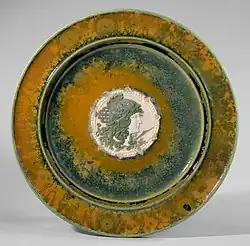 Grün-orange farbig glasierter Teller mit eingelassenem Kopfmedaillon