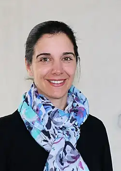 Eine Frau mit schwarzem Pullover, dunklen nach hinten gebundenen Haaren und einem großen Tuch in blauen Farben um den Hals