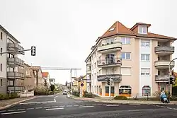 Links und rechts einer kleinen Straße mit dem Schild Tempolimit 30 sind Häuser mit Balkonen in gutem Erhaltungszustand zu sehen.