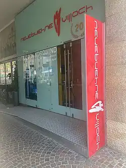 Man sieht den Eingangsbereich der neuebuehnevillach mit Glastüren, dem Schaukasten und dem Logo der neuebuehnevillach