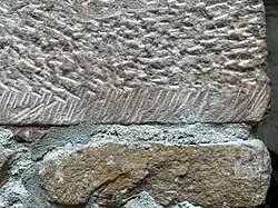 Der obere Stein weist deutliche Bearbeitungsspuren, d.&nbsp;h. eine Faktur auf. Der untere Stein ist unbearbeitet und zeigt eine körnige, unregelmäßige Textur.