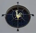 Das Fenster über der Empore ist nach außen vergittert. Besonders auffällig ist der goldene Hahn, der an die Verleugnung Petri erinnern soll.
