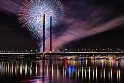 Nachtaufnahme einer Feuerwerksexplosion über dem Rhein in Düsseldorf, im Vordergrund eine filigranen Schrägseilbrücke, die Rheinkniebrücke, als Schattenriss.