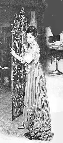 Porträt von Jeanne de Flandreysy in einem langen Kleid und mit hochgestecktem Haar. Sie hält ein reich verziertes Eisengitter in den Händen. Ihr Blick ist nach links gerichtet.