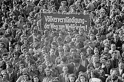 "Schwarz-Weiß-Fotografie zeigt Menschenmenge und ein Plakat mit der Aufschrift: Völkerverständigung – Der Weg zum Weltfriedenǃ"