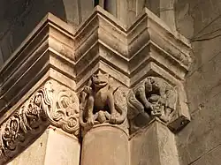 Romanischer Fries mit drei Fabelwesen (auf Rundsäule) und zwei Männern beim Glücksspiel mit Würfeln (auf eckiger Säule)