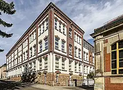 Panoramablick auf viergeschossiges heutiges Schul- und ehemaliges Fabrikgebäude.