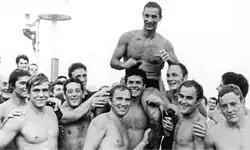 Auf dem Schwarz-Weiß-Foto ist eine Wasserballmannschaft zu sehen, die einen der ihren auf den Schultern trägt.