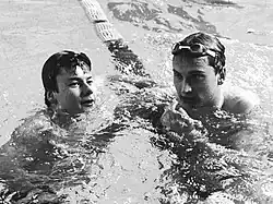 Auf diesem Schwarzweißfoto stützen sich zwei Schwimmer nach der Zielankunft auf der Trennleine ab. Beide haben ihre Schwimmbrille nach oben geschoben.